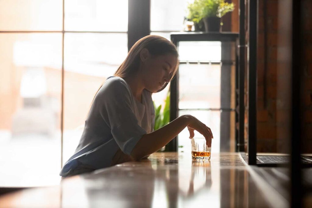 A woman sitting at a bar alone drinking, self reflecting on if she is an alcoholic