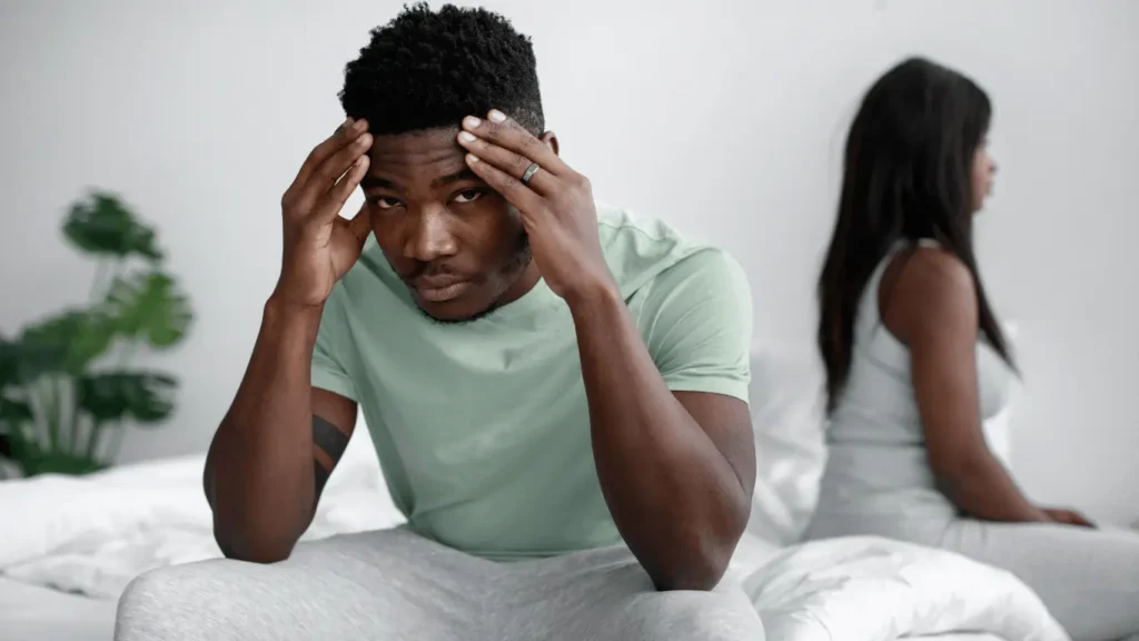 A person living with addiction and mental health concerns sits on a bed with their hands on their head
