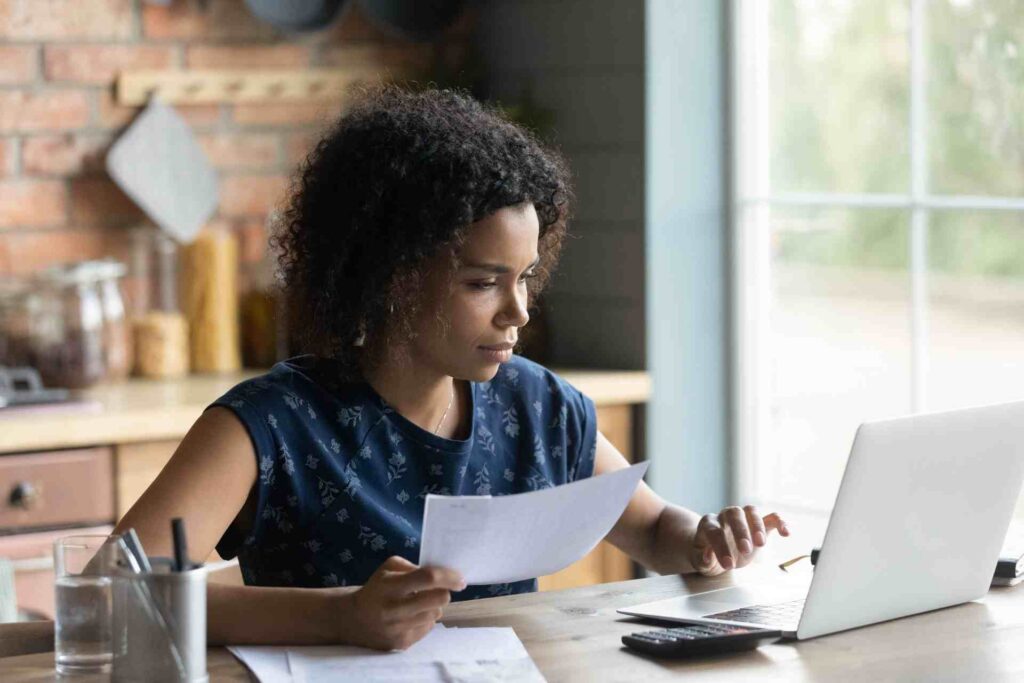 How Insurance Coverage Works for Addiction Treatment in Florida is shown by a woman reviewing paperwork and using her laptop in a home office.